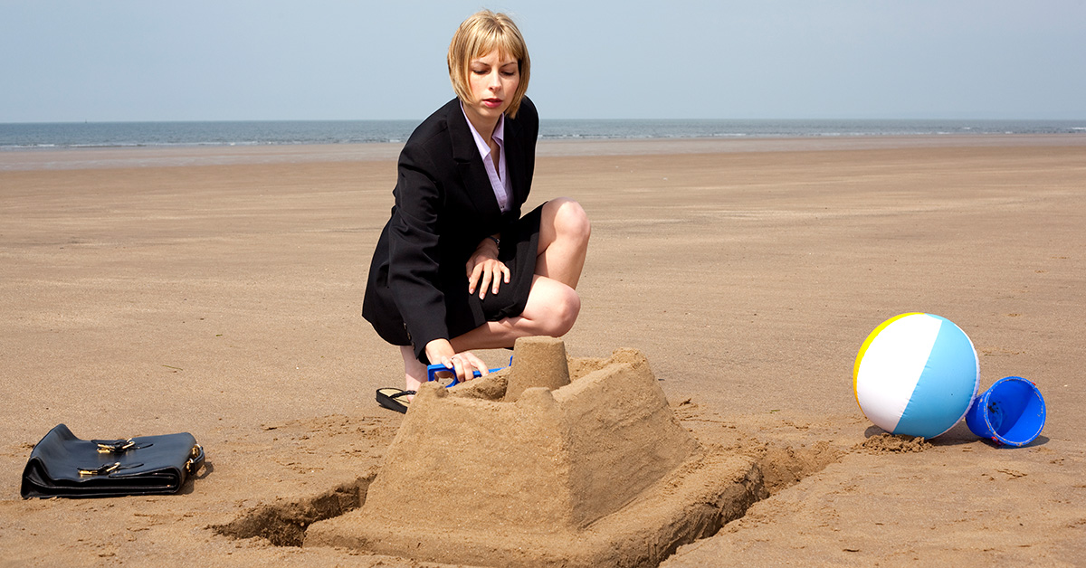 Business woman completing a sandcastle on a beach